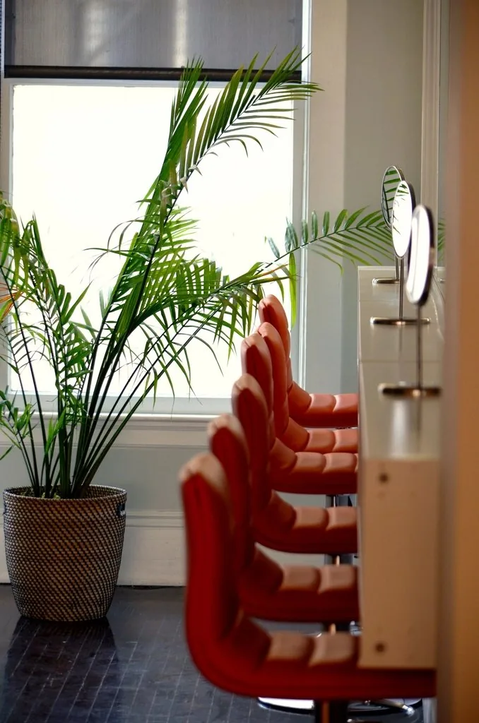 De rode kappersstoelen van Salon Camille op een rij bij het raam, in ruim daglicht