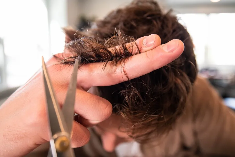 Close-up van handen die een pluk haar tussen de vingers nemen en knippen